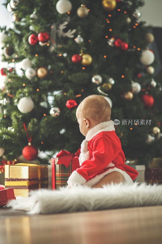 Baby girl sitting by Christmas tree and presents